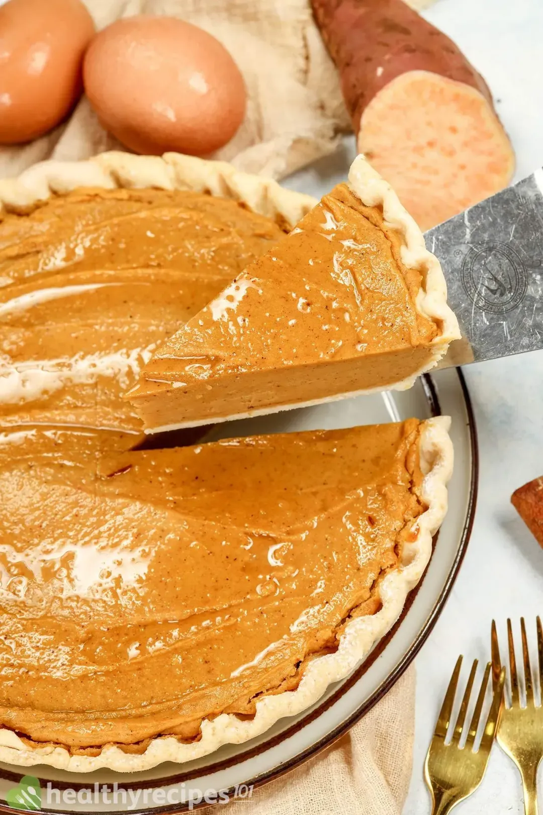 A slice of sweet potato pie being taken from a whole pie with a cake spatula