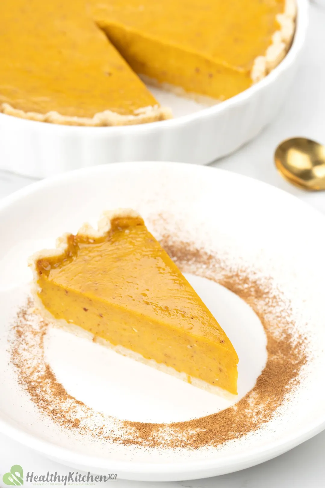 A slice of pumpkin pie on a white plate placed near a whole pie.