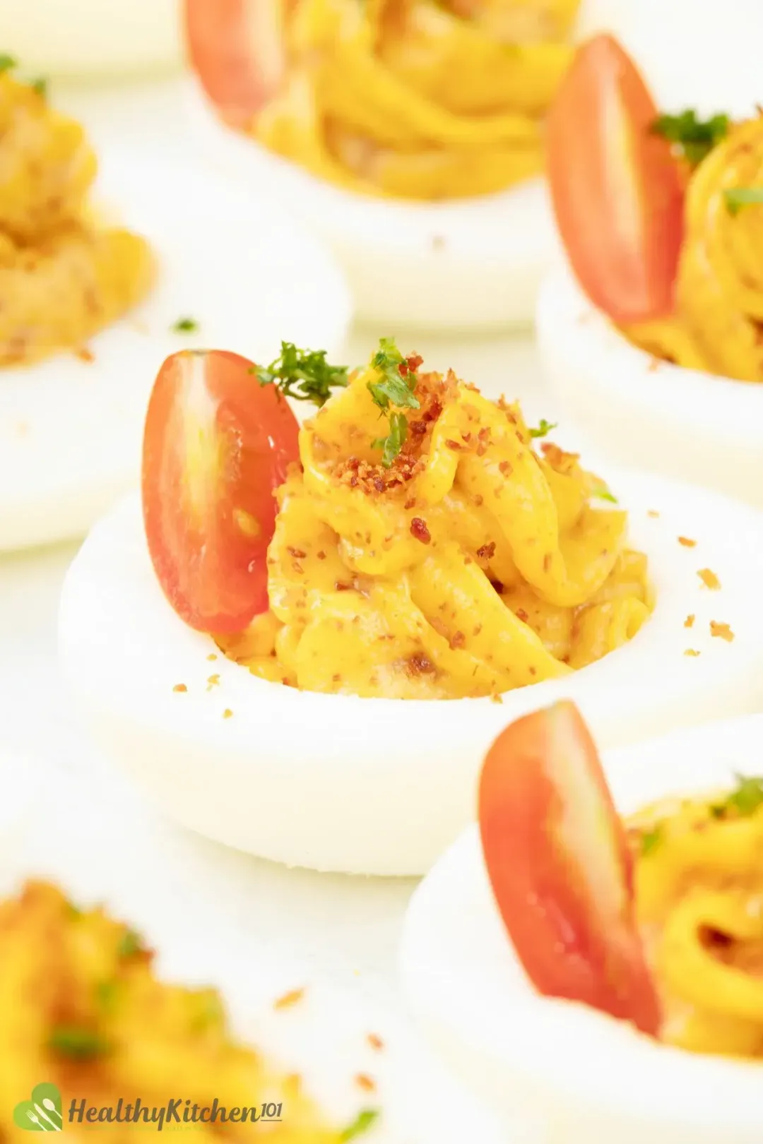 A close-up shot of some deviled eggs, with half a cherry tomato, spices, and herbs on top