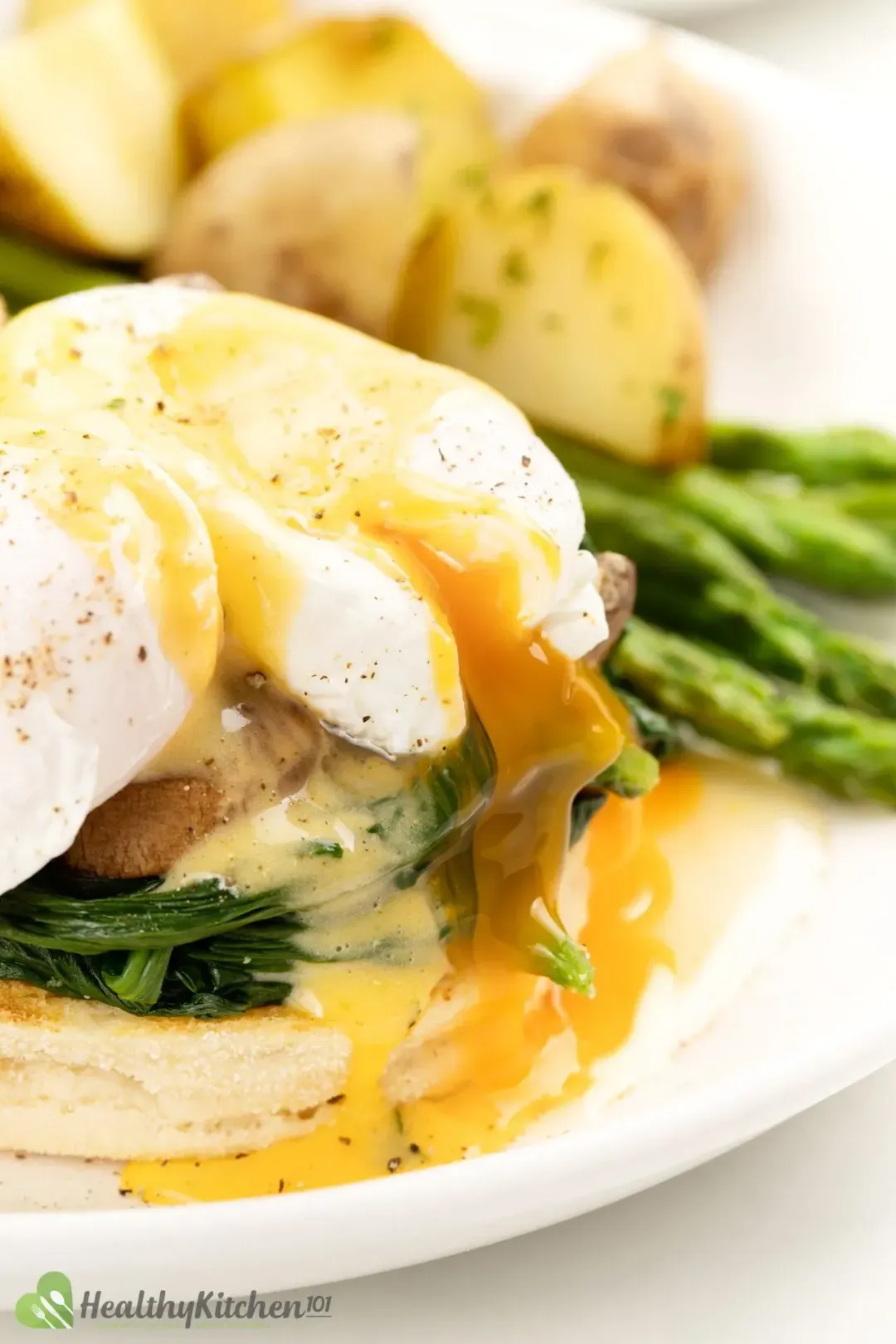 A close-up shot of poached eggs drenched in hollandaise sauce over cooked and squeezed spinach and half an English muffin