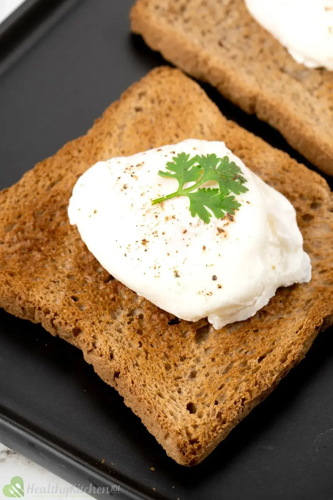 A slice of brown toast with a poached egg on top, topped with pepper and a cilantro sprig