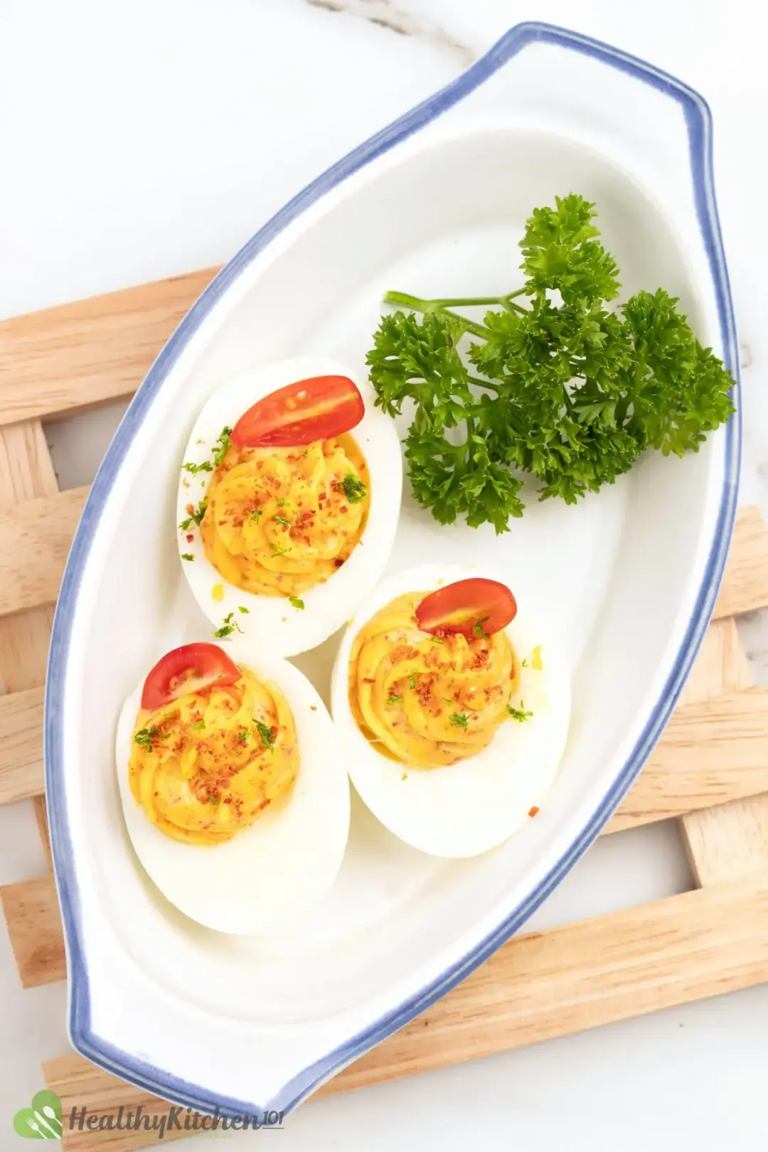 Three deviled eggs, each with half of a cherry tomato and next to green parsley