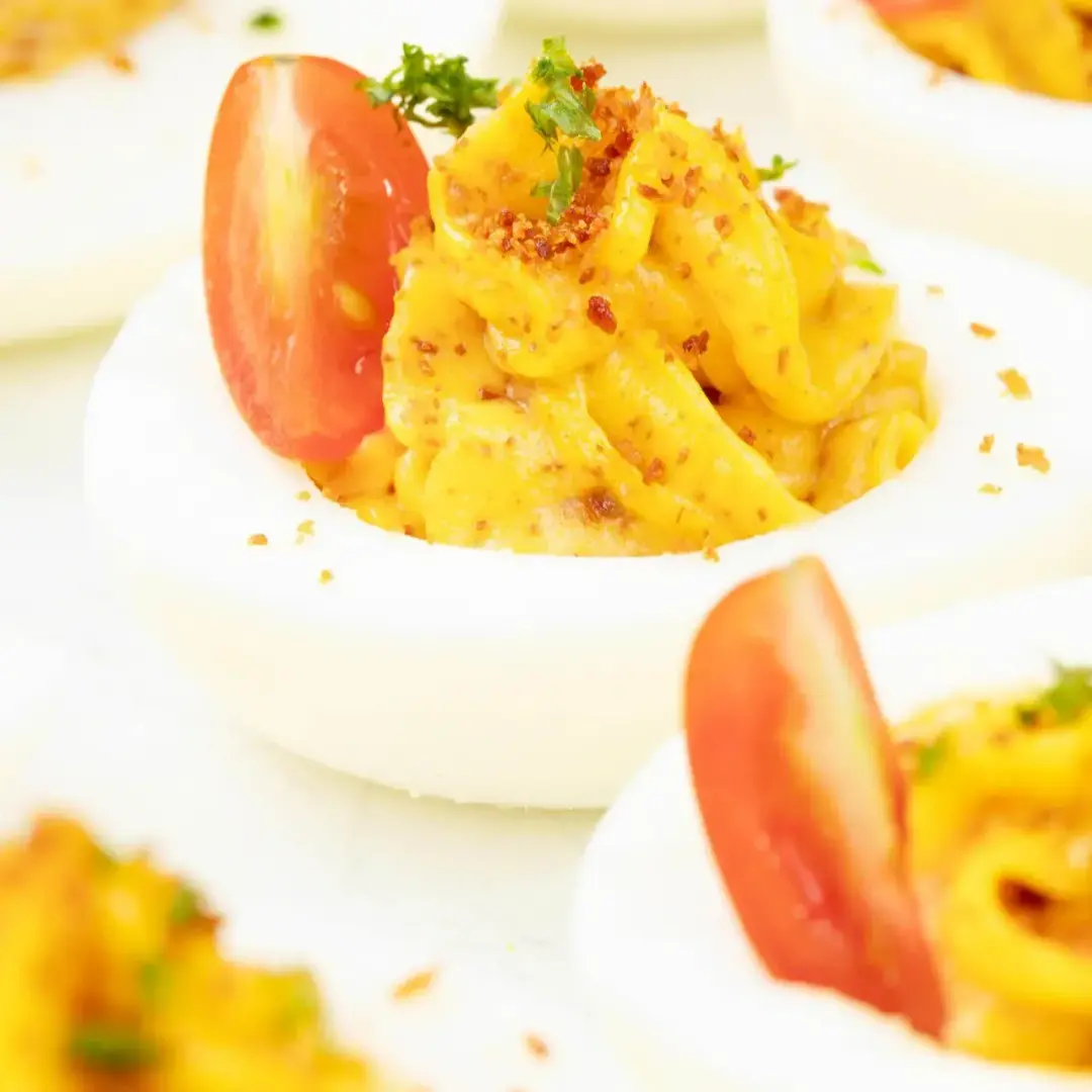 A close-up shot of some deviled eggs, with half a cherry tomato, spices, and herbs on top