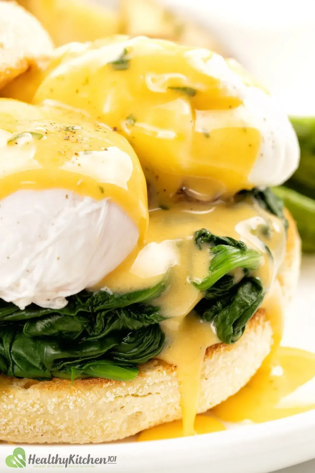 A close-up shot of poached eggs drenched in hollandaise sauce over cooked and squeezed spinach and half an English muffin