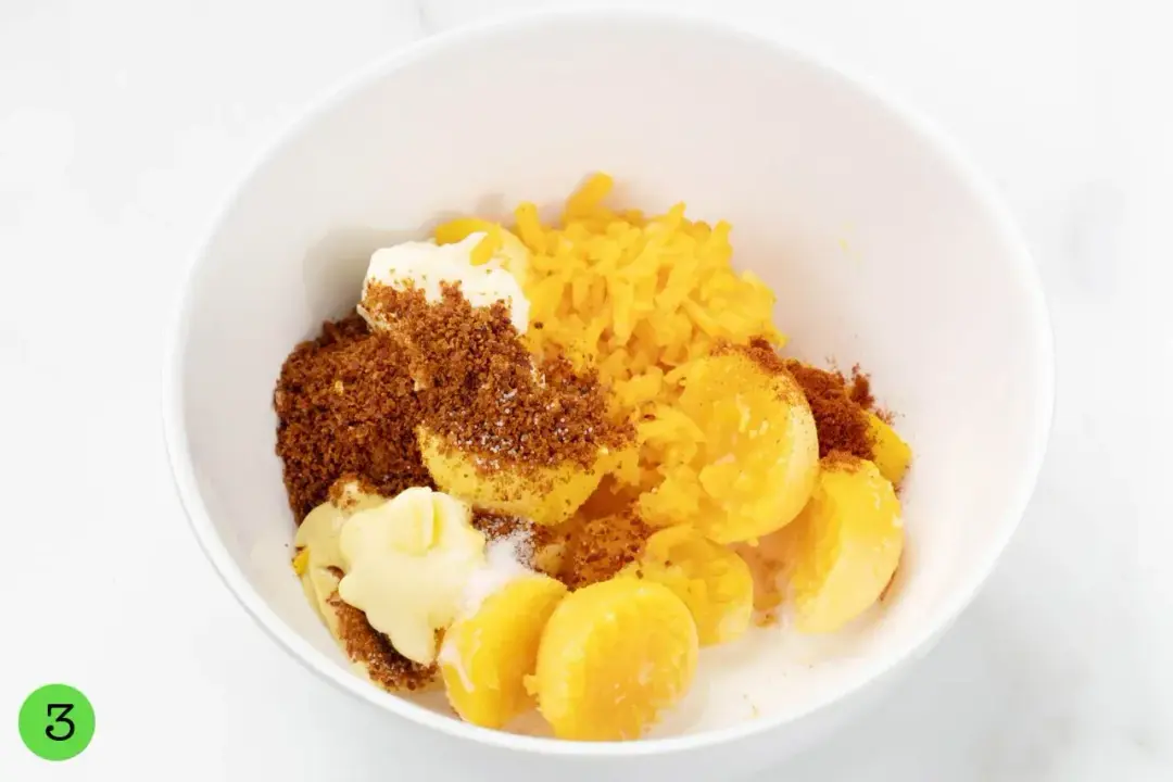 Boiled egg yolks mashed in a white bowl with cheese, bacon crumbles, mayo, and spices