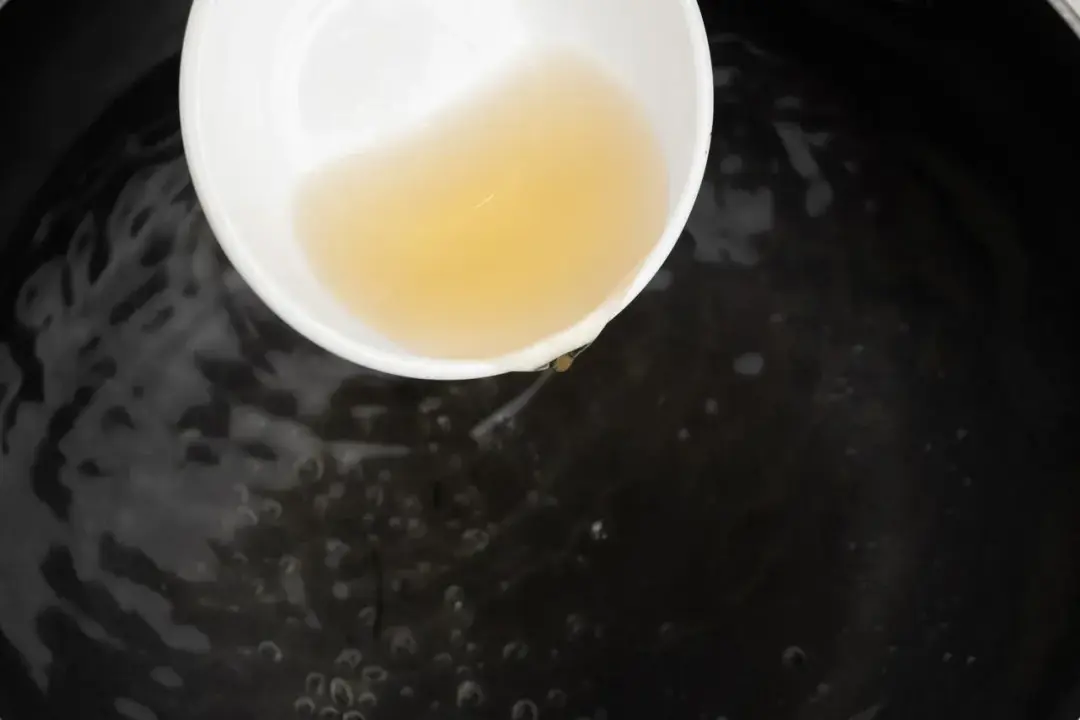Vinegar in a white bowl pouring into a black pot of water