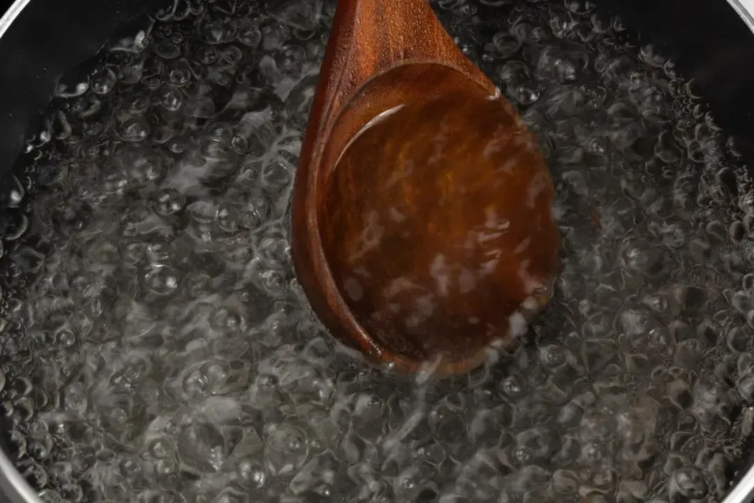 A wooden ladle dunked into a boiling pot of water