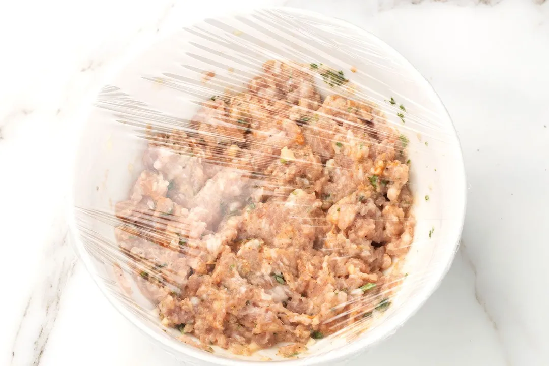 mixed ground pork with seasoning in a bowl covered by plastic wrap