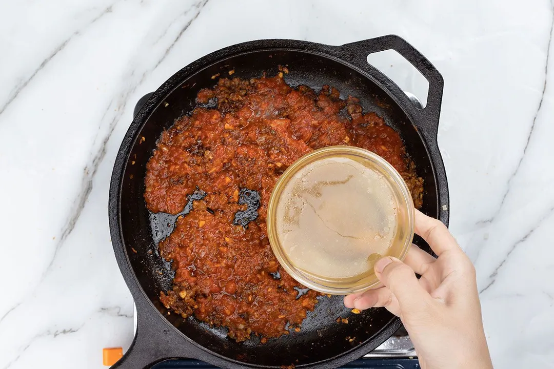 hand holds a bowl of broth on top of a pan of curry sauce