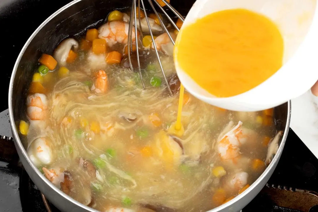 pouring beaten eggs from a bowl into a skillet of soup