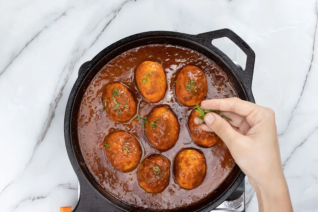 sprinkle cilantro on top of a skillet of cooked eggs curry