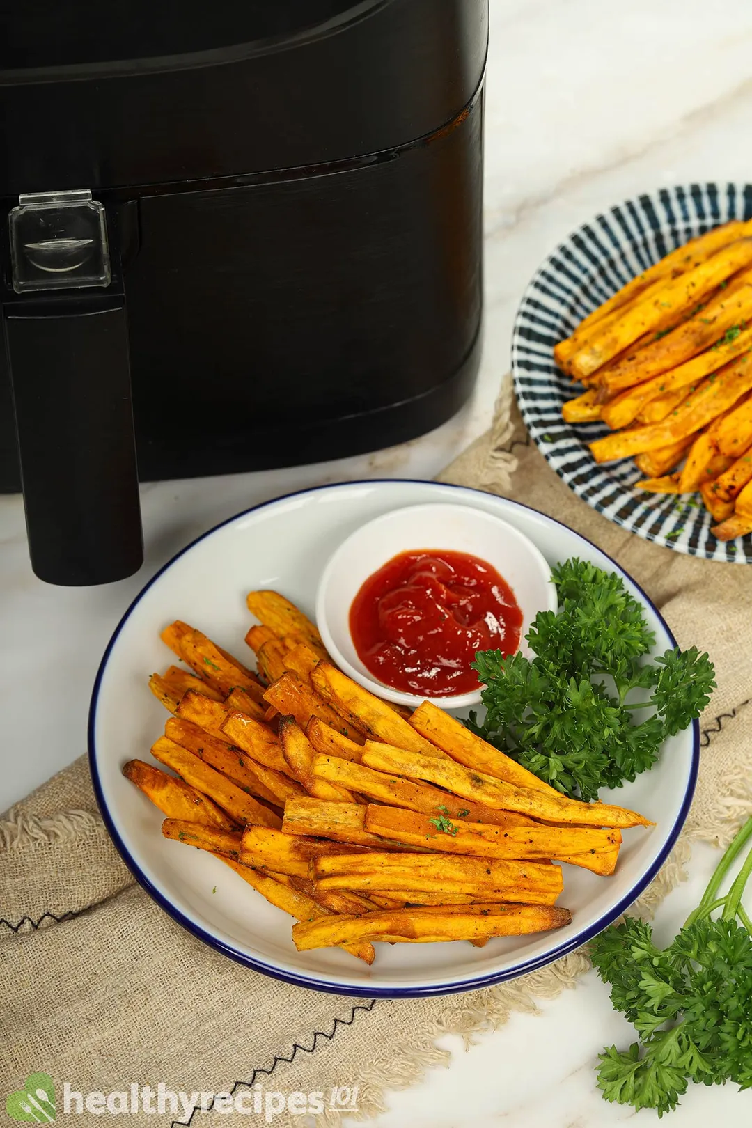 two plates of cooked sweet potato sticks next to an air fryer