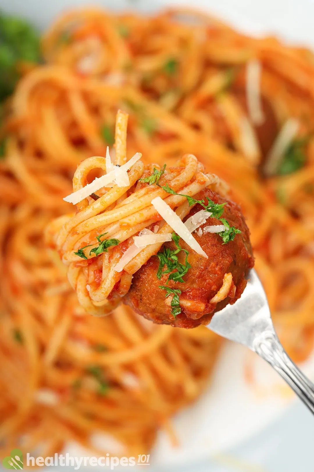 A fork piercing into a chickpea meatball wrapped in spaghetti pasta.
