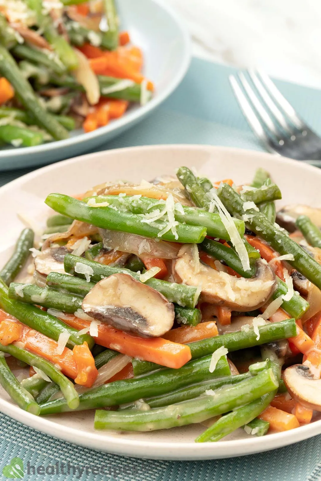 Two plates of sauteed green beans, carrots, and mushrooms.