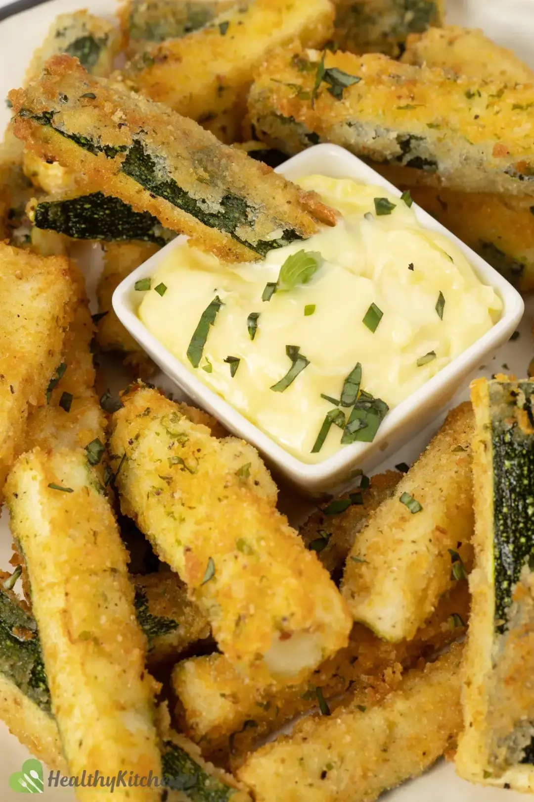 A mayonnaise dipping put inside a plate of zucchini fries, garnished with chopped herbs
