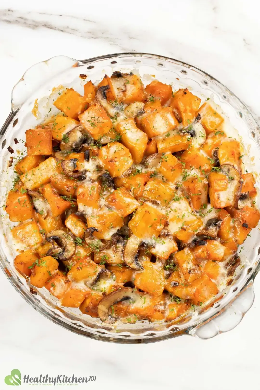 A round casserole dish filled with baked butternut squash and mushrooms, topped with melted cheese