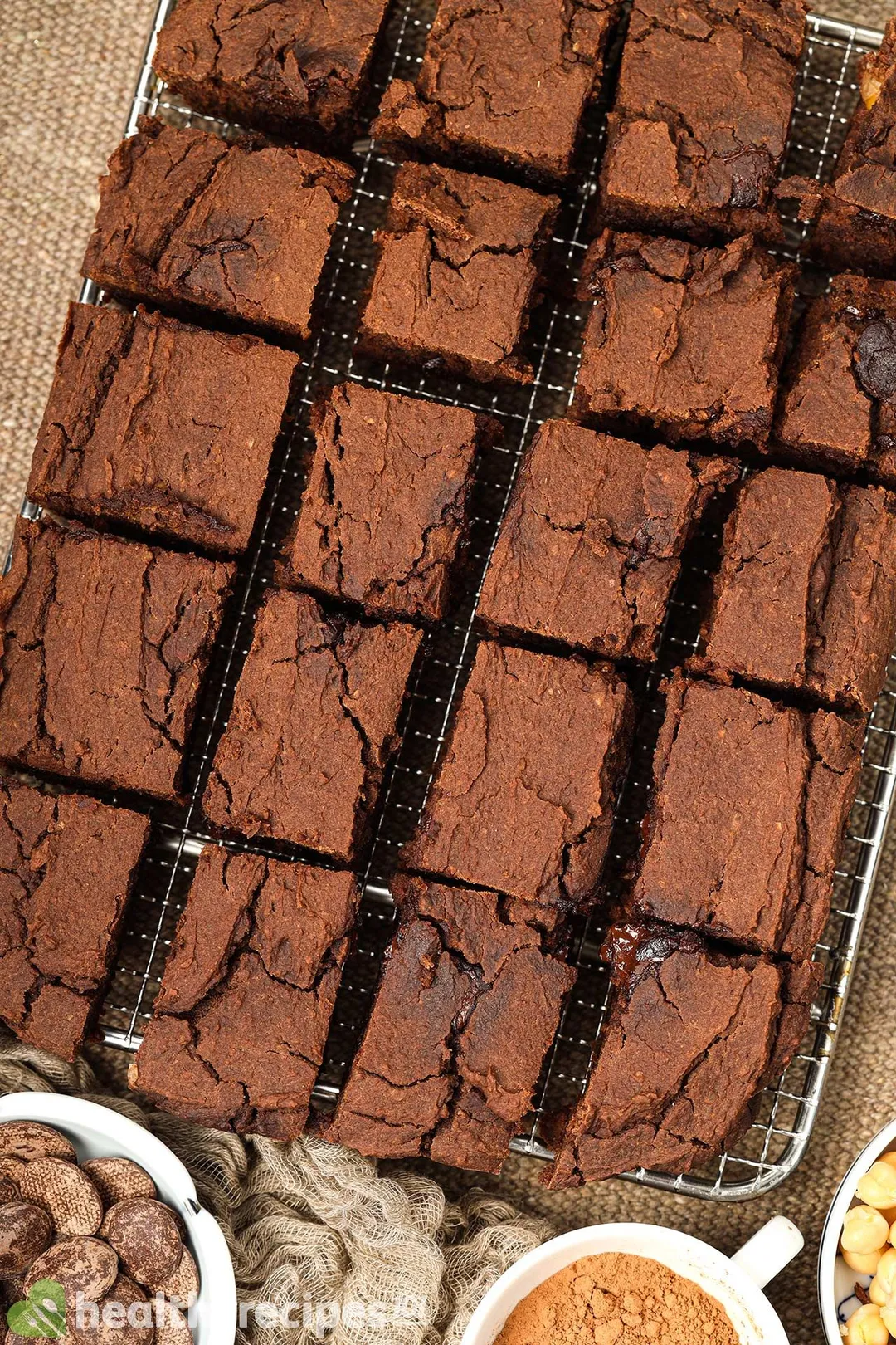Squares of chickpea brownies laid on a cooking rack near a disk of chocolate chips.