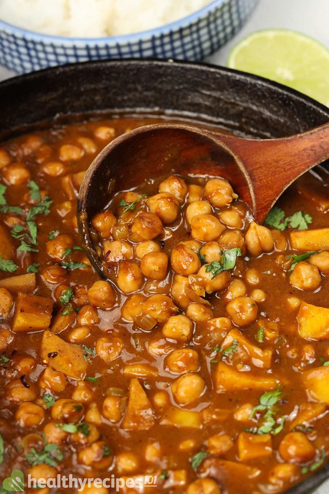 A wooden laddle scooping into a skillet filled with chickpea curry.