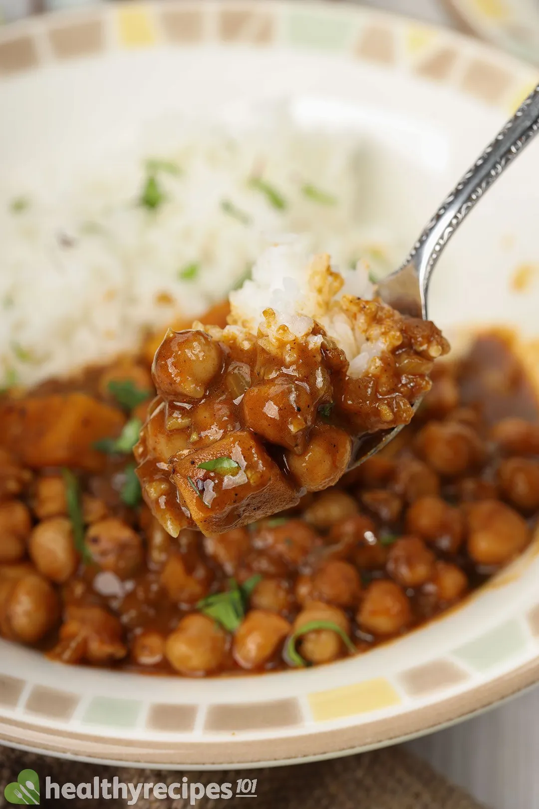 A spoon scooping up chickpea curry and some white rice.