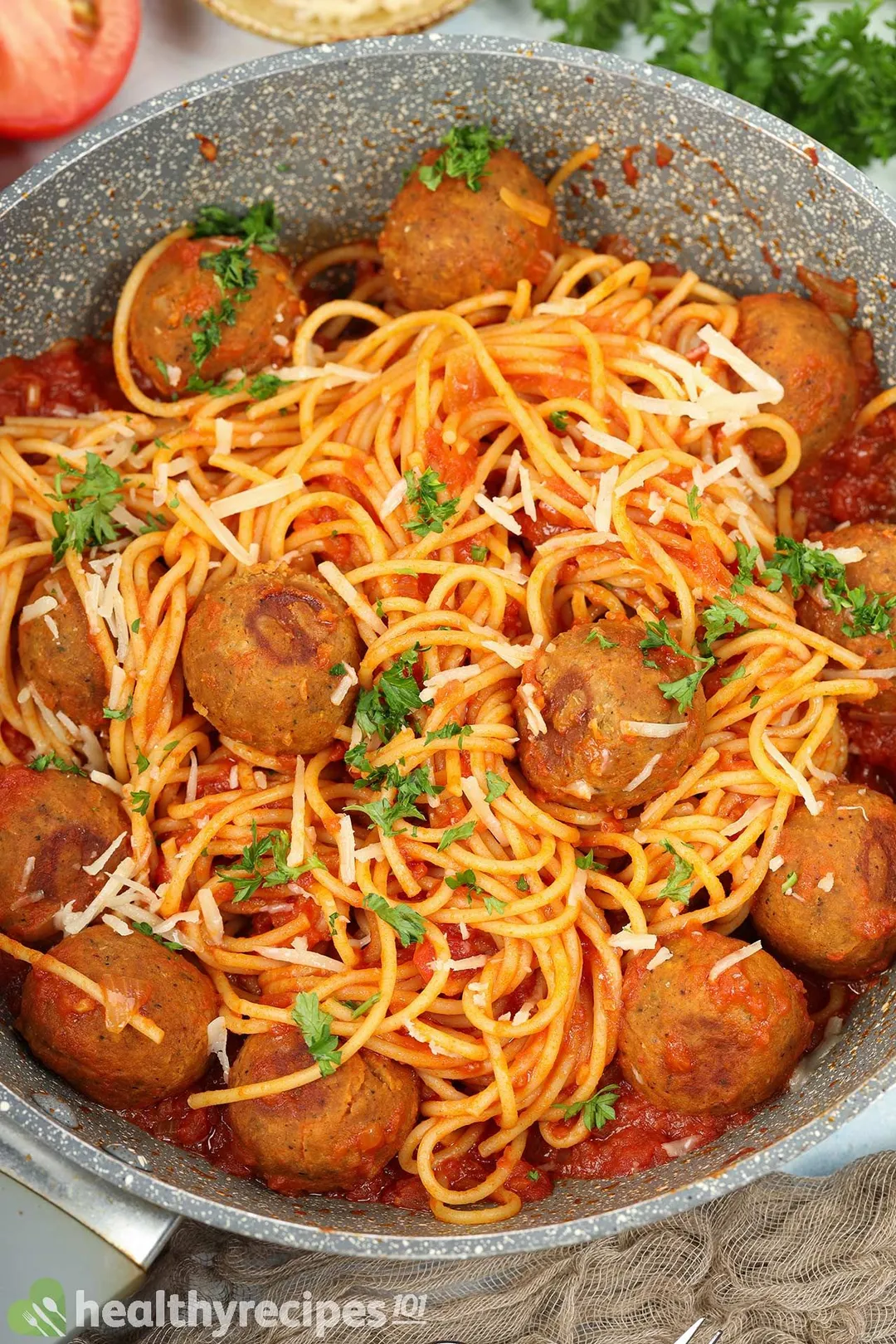 A pan filled with chickpea meatballs and spaghetti pasta covered in tomato sauce and garnished with chopped parsley.