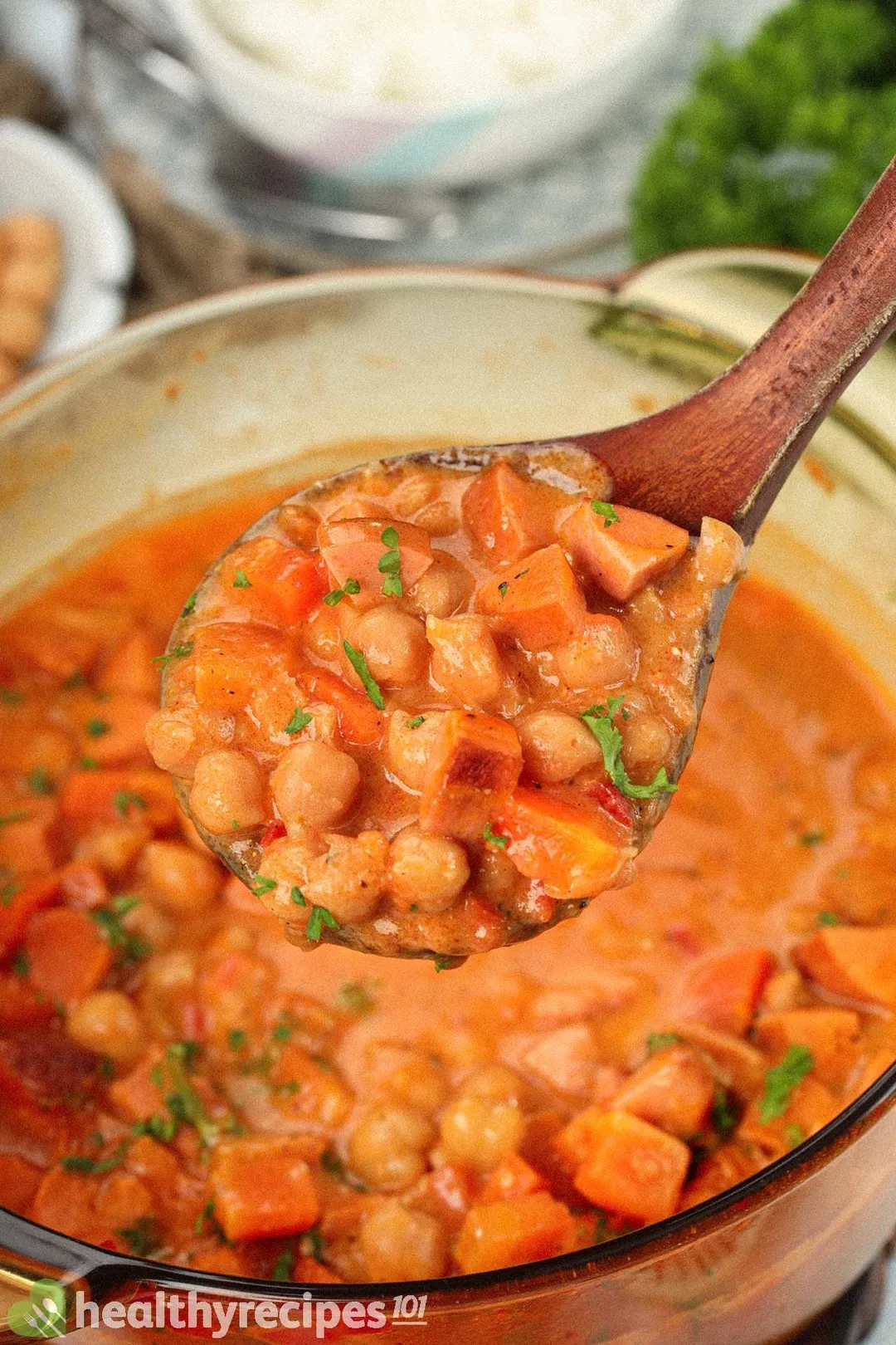 A wooden laddle scooping chickpea stew from a pot filled with chickpea stew.