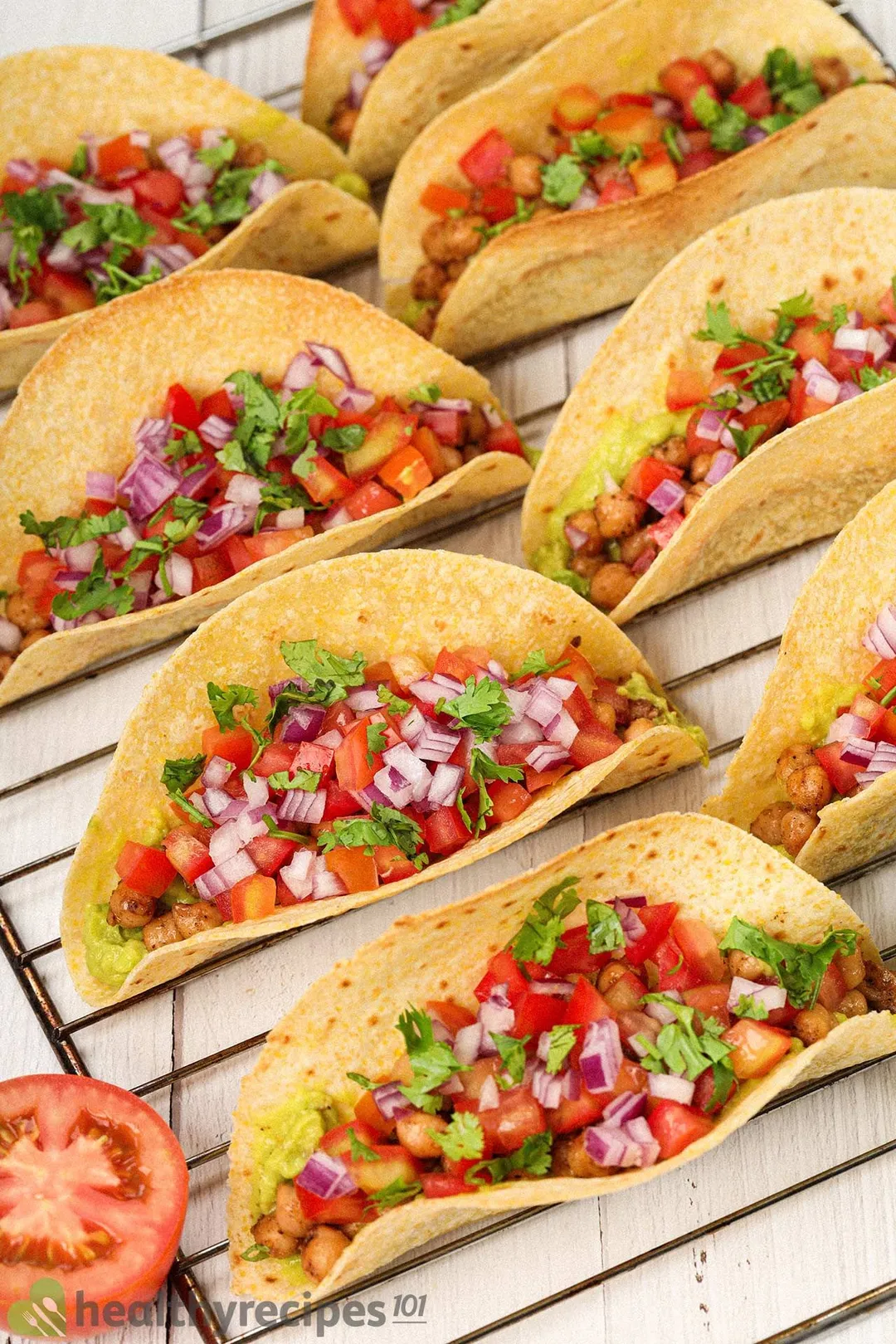 Chickpea tacos lined up on a rack with half a tomato laid near by.