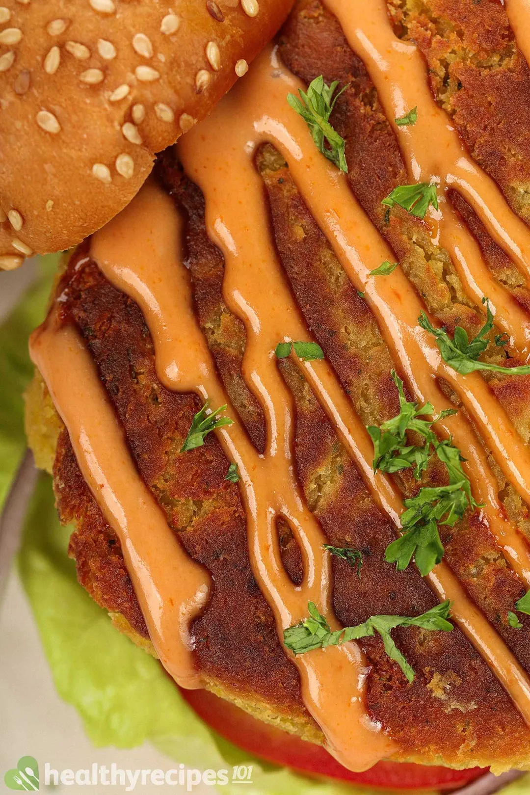 A close-up shot of a chickpea pattie drizzled with an orange sauce and garnished with chopped parsley.