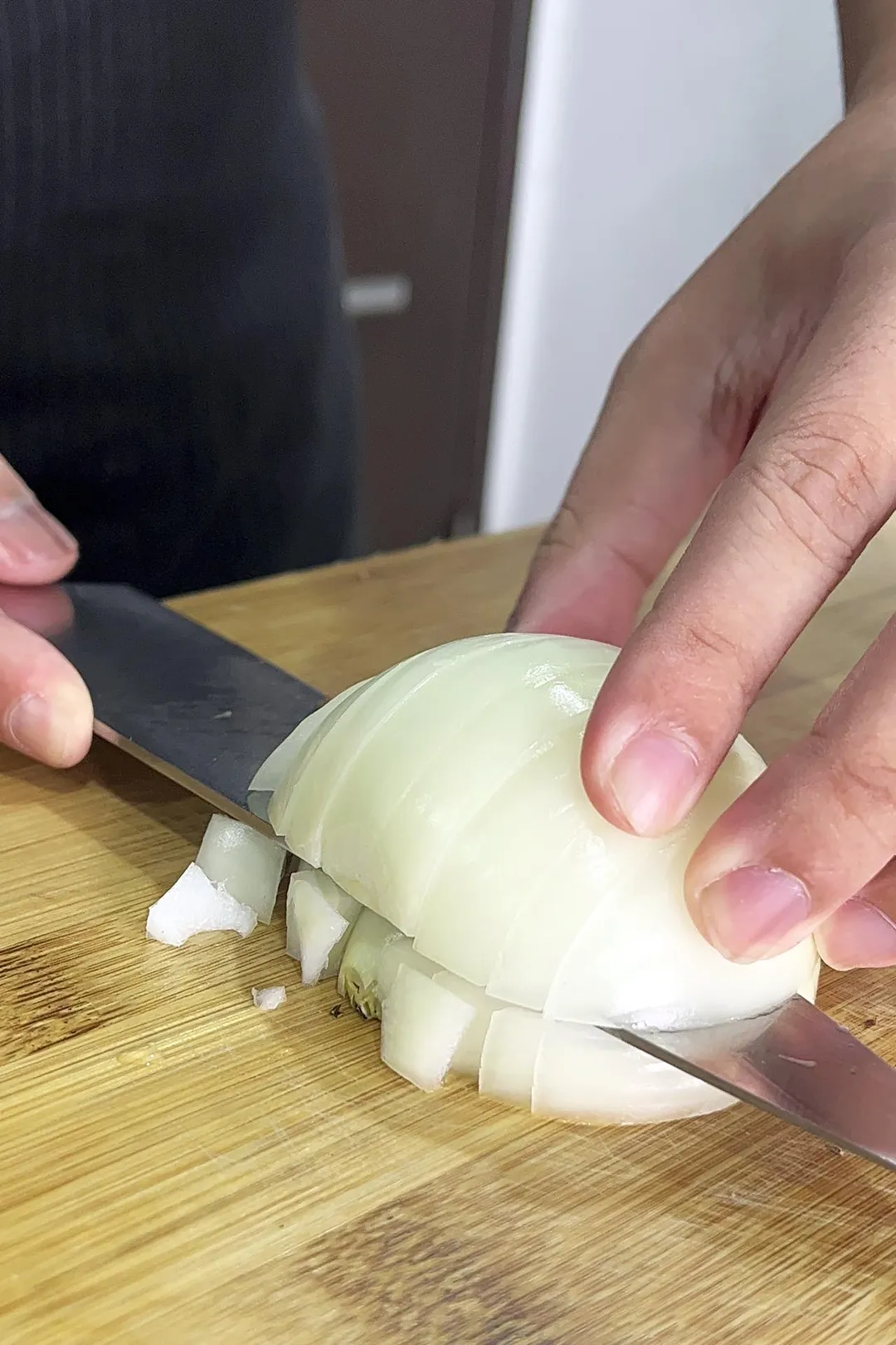 One hand holds half an onion, the other uses a knife to cut it