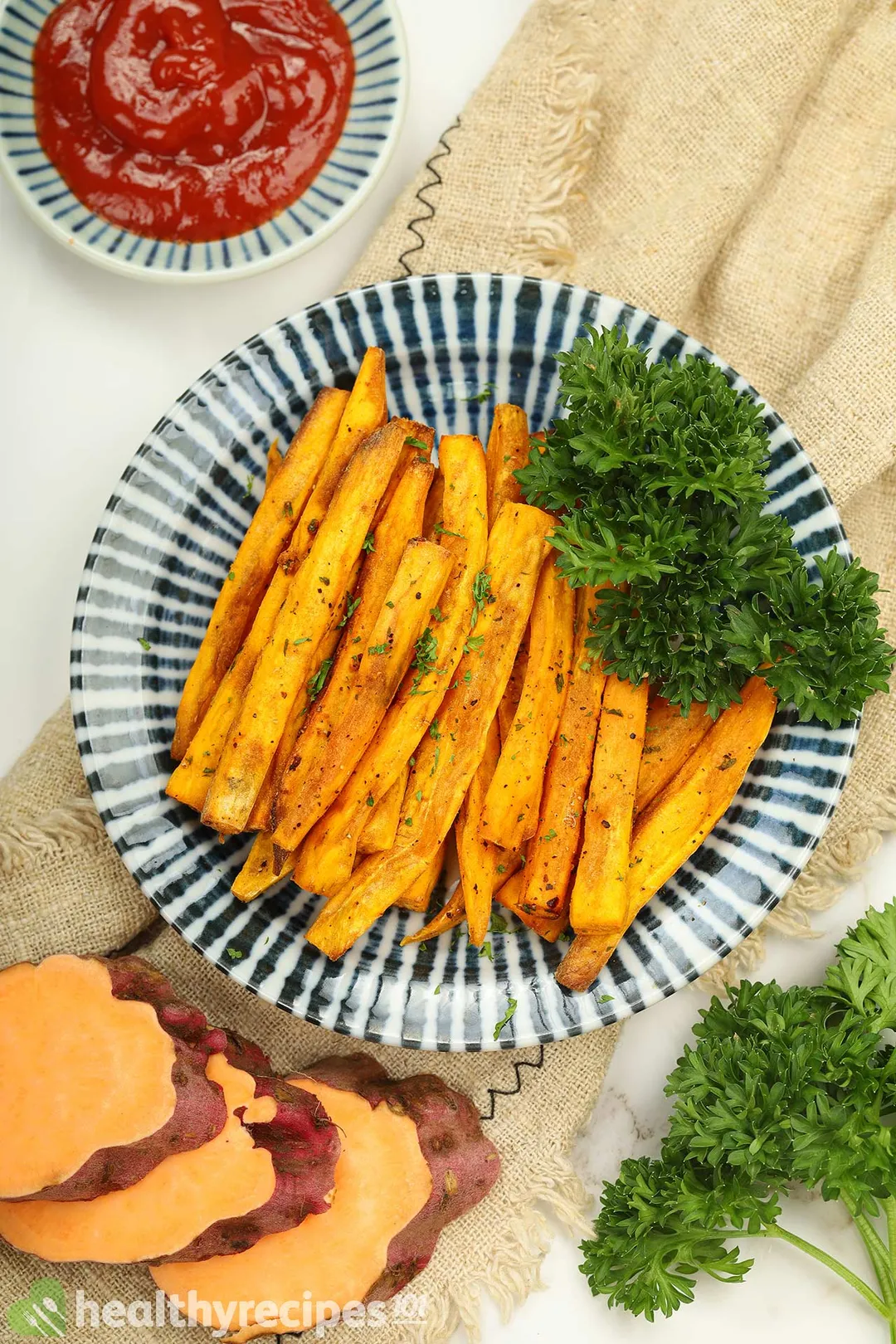 top view of a plate of cooked air fryer sweet potato sticks decorated with sweet potato slices, a small bowl of ketchup