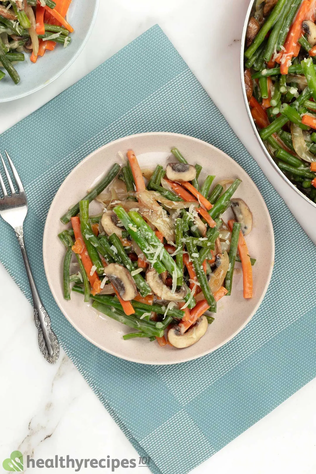 A plate of sauteed green beans placed on a blue cloth and next to a fork.