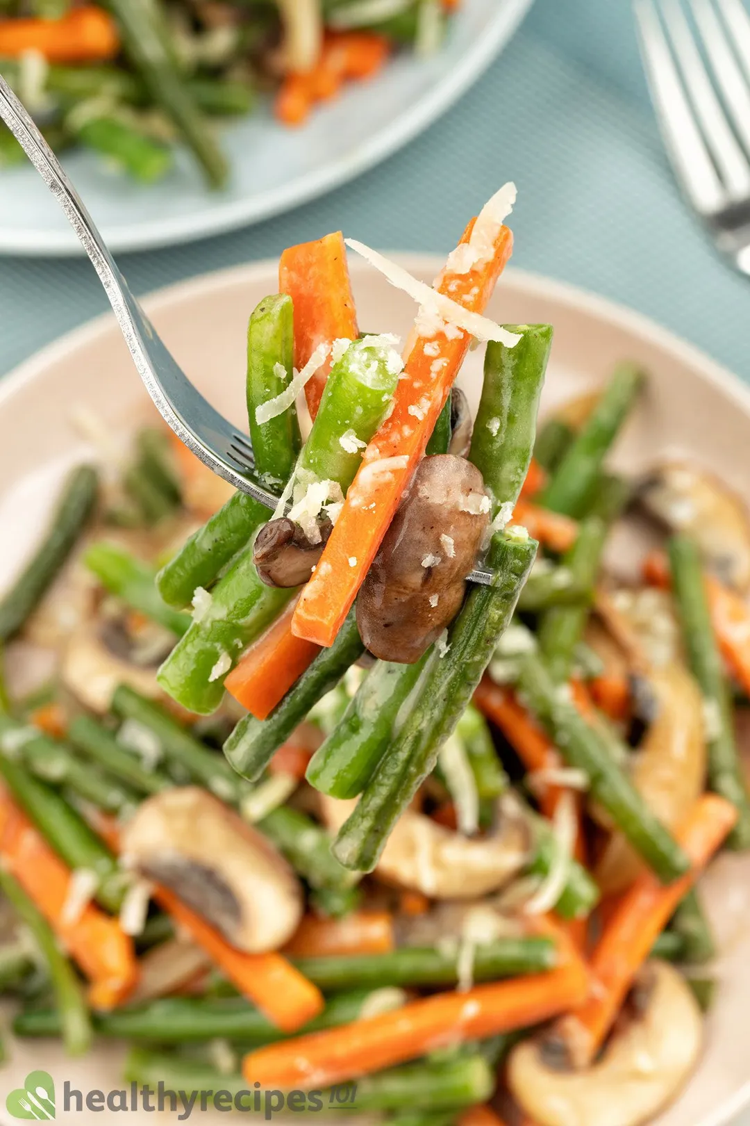 A fork piercing into green beans and julienned carrots.