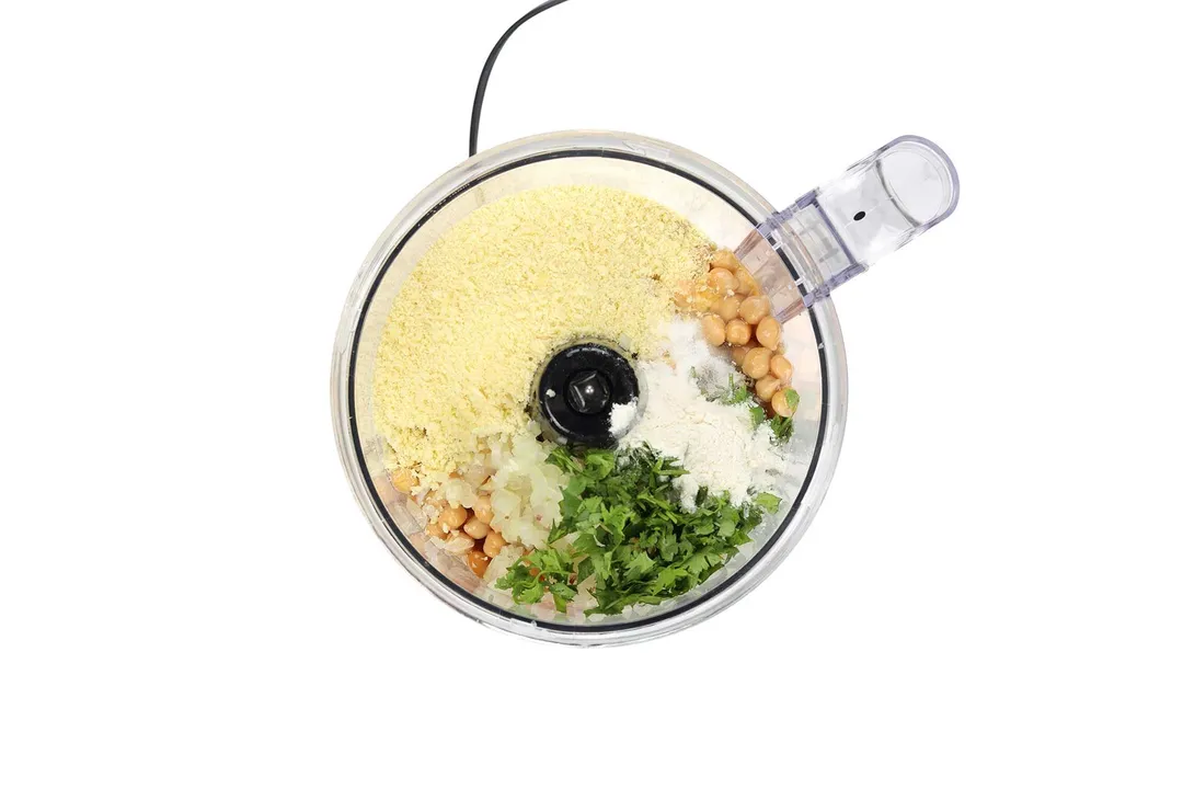 A food processor filled with breadcrumbs, chickpeas, diced onion, and chopped coriander.