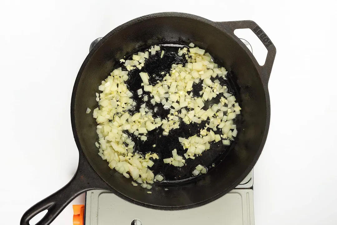 A skillet cooking diced onion on a portable gas stove.