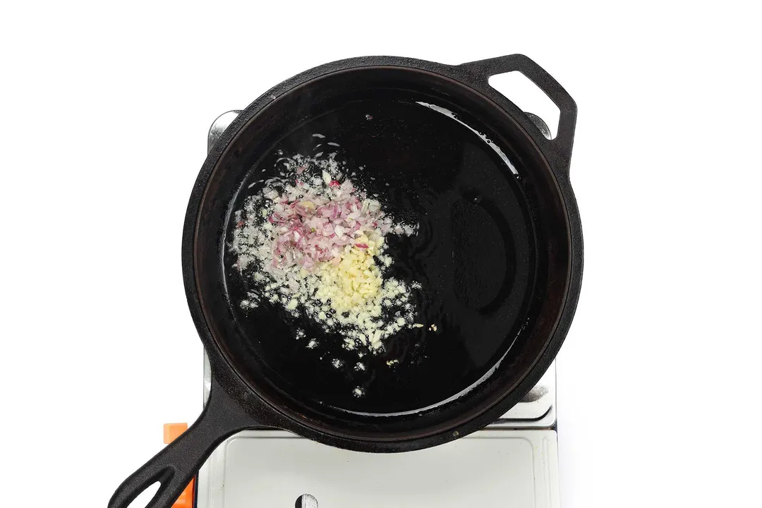 A skillet cooking minced shallot and minced garlic on a portable stove top