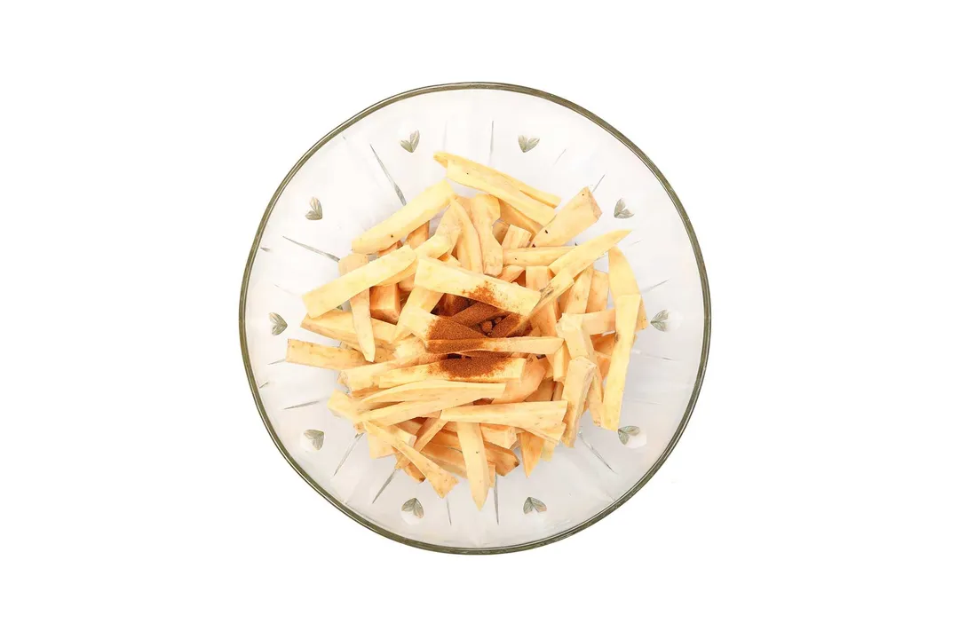 A pile of uncooked sweet potato sticks with some seasonings in the center laid on a round white plate.