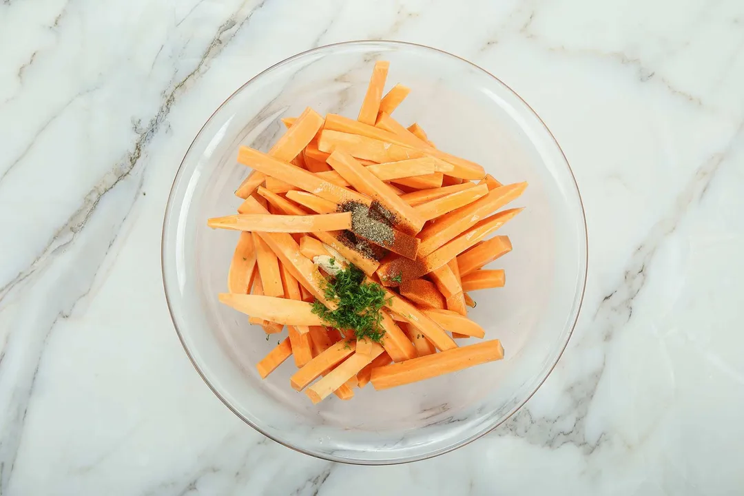 sweet potato sticks and seasoning in a glass bowl