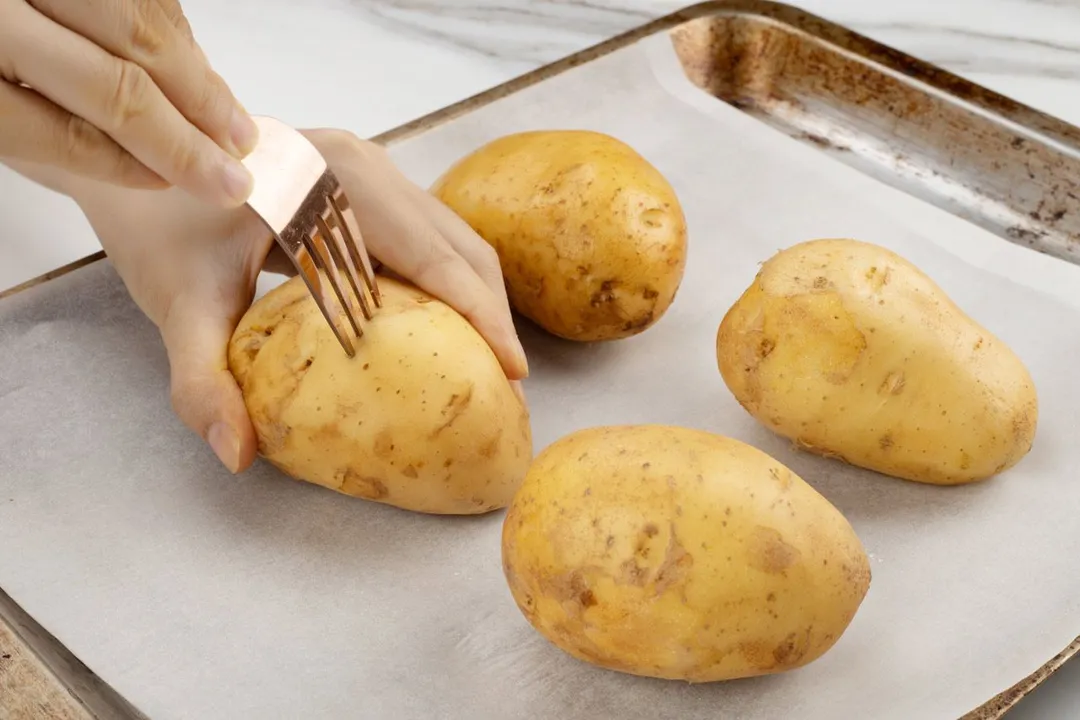 hand holds a fork to pierce the potato skin