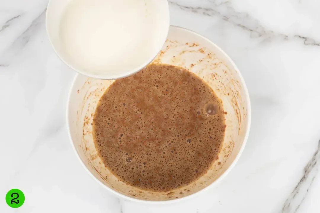 A bowl of milk about to be poured into a mixture of beaten eggs and spices