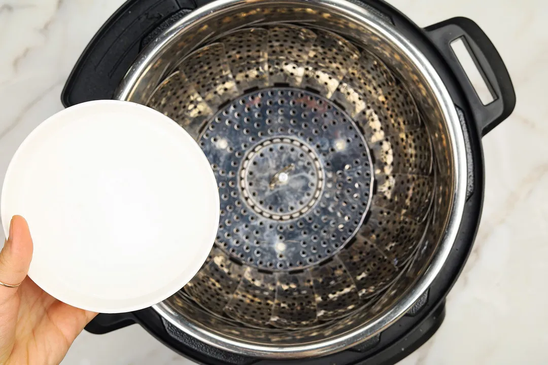 hand holds a bowl of water on top of an instant pot