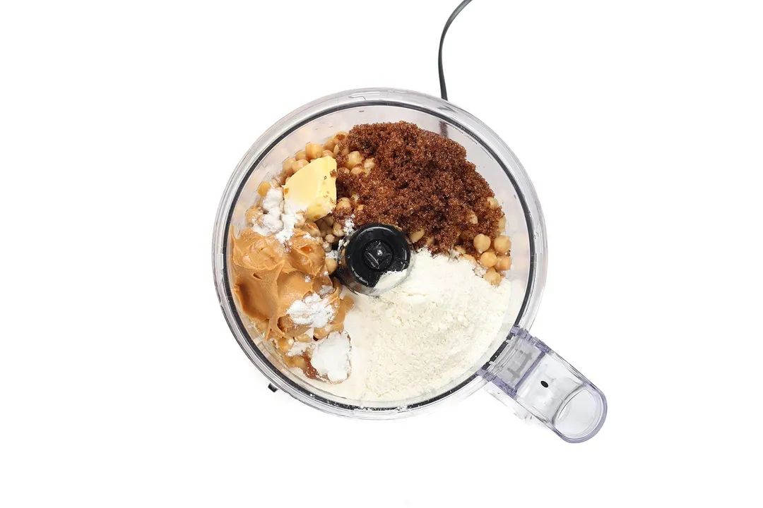 A food processor containing brown sugar, chickpeas, butter, flour, and peanut butter.