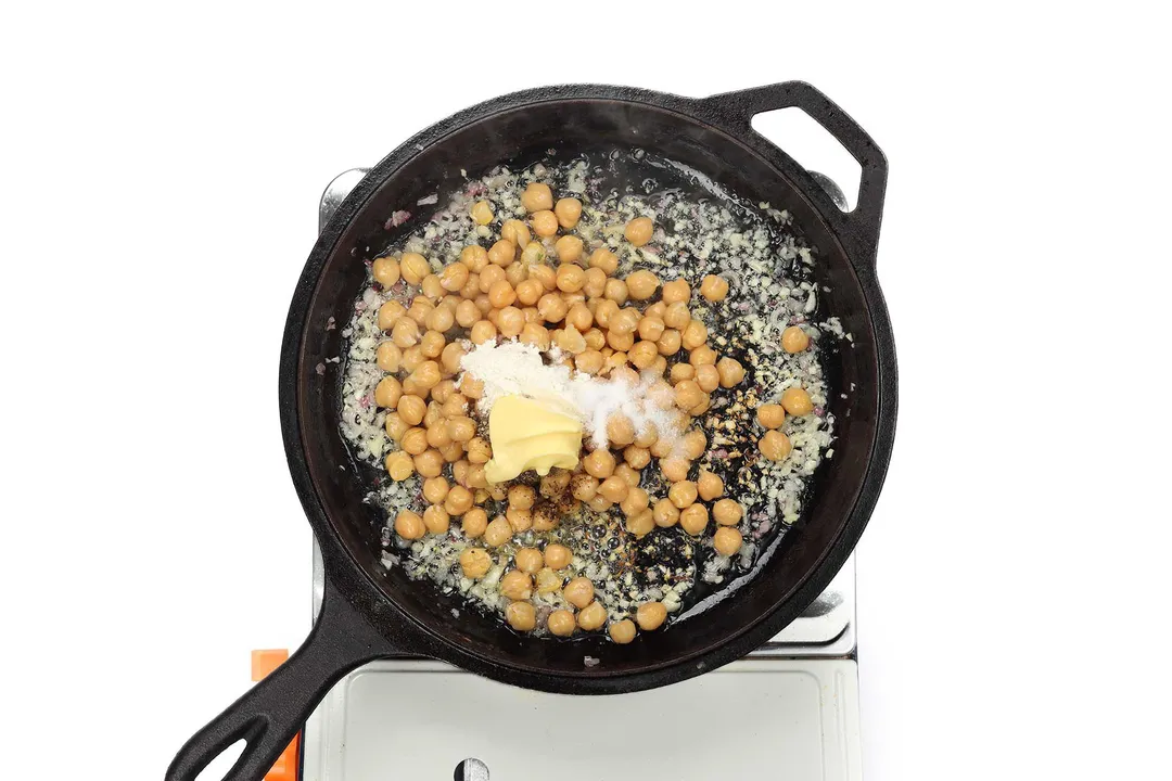 A skillet cooking chickpea with butter, minced garlic, and minced shallots with spices and seasonings.