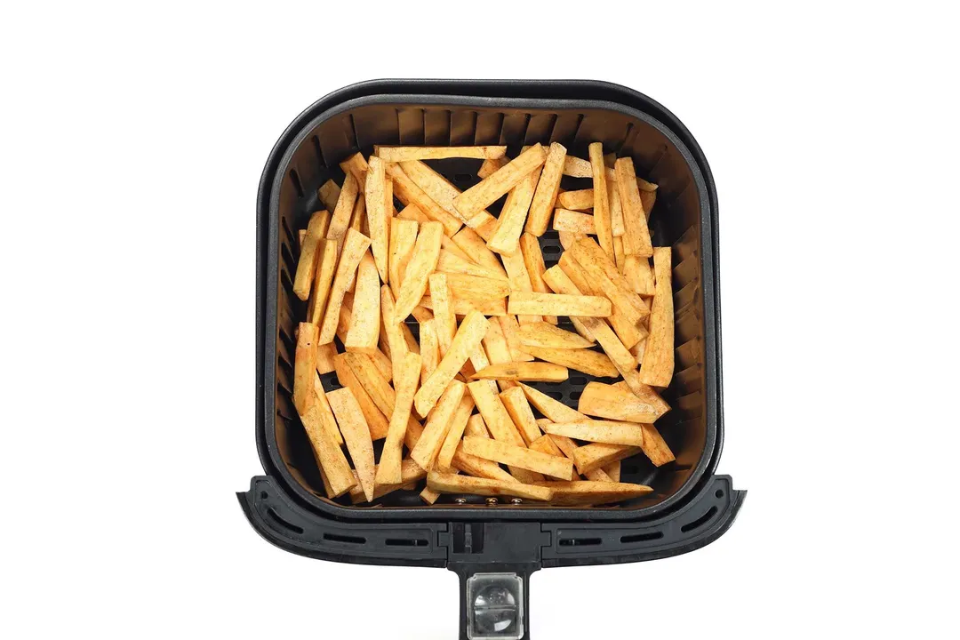 An air fryer basket filled with uncooked sweet potato sticks.
