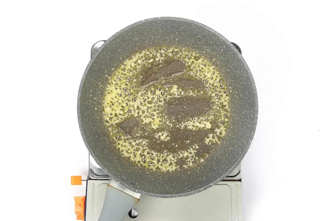 A pan cooking minced garlic on a portable gas stove.