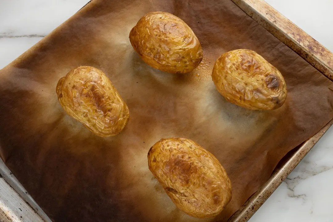 four baked potatoes on a baking tray