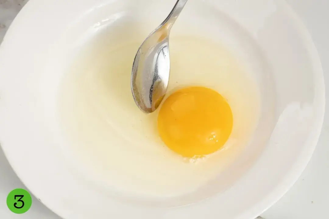 A cracked egg in a white plate with a silver poon dunked in