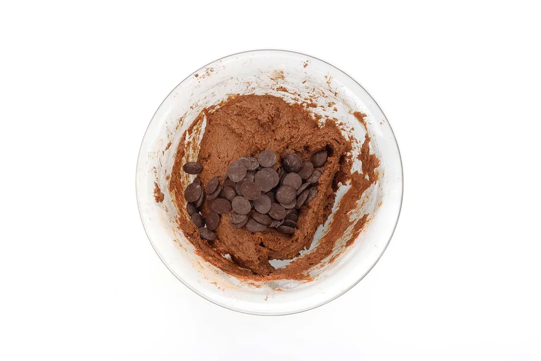 A glass bowl containing a blended mixture for chickpea brownies and chocolate chips.