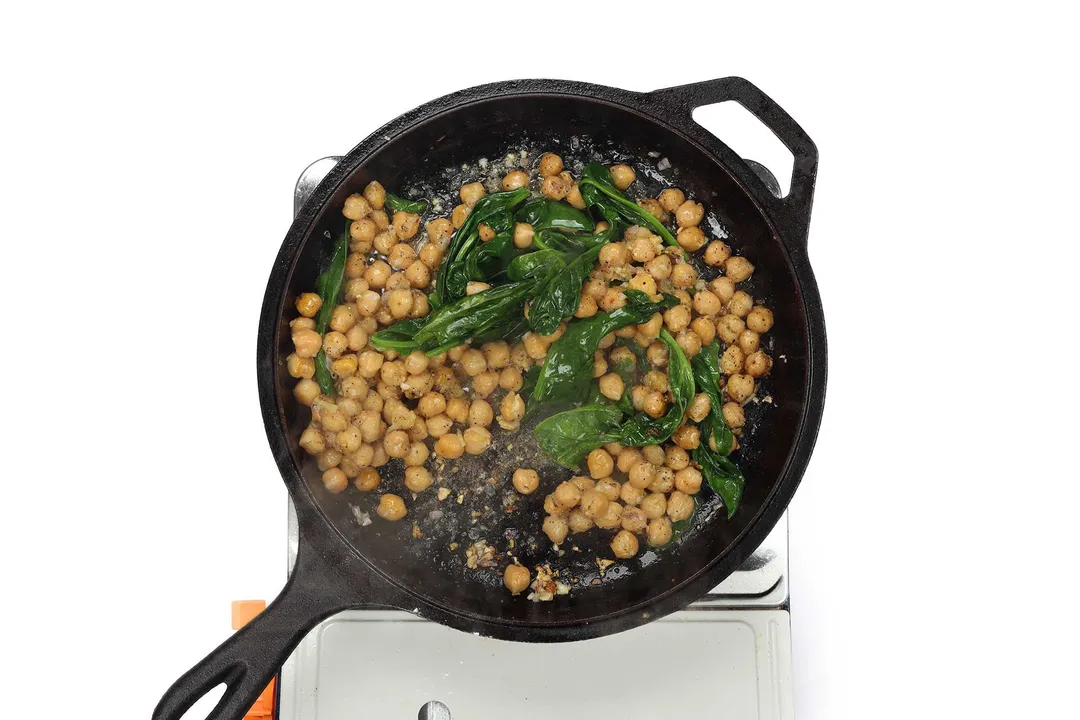 A skillet cooking chickpeas and spinach on a portable gas stove.