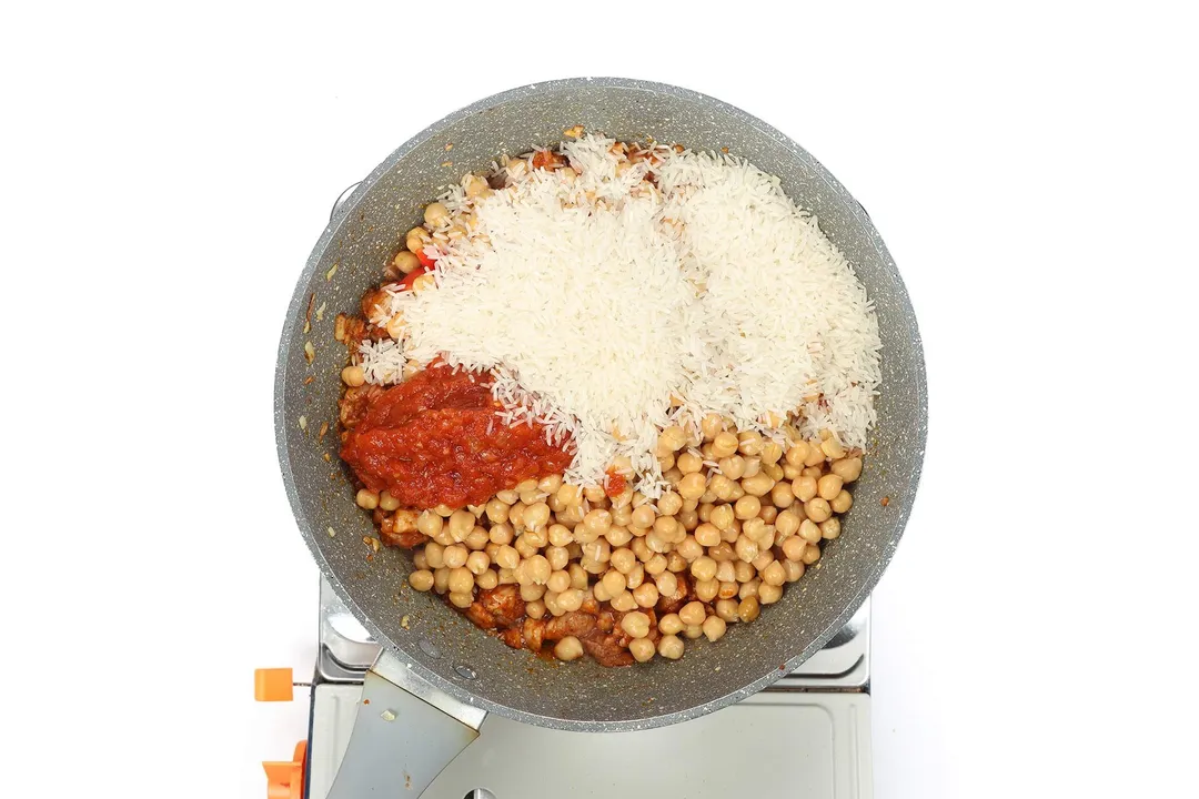 A large pan cooking white rice, chickpeas, and tomato sauce on a portable gas stove.