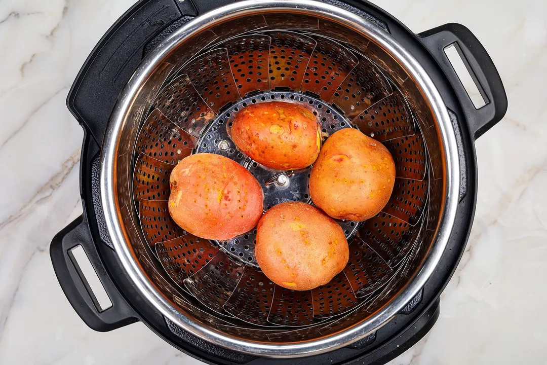 four potatoes on a steamer basket in an instant pot