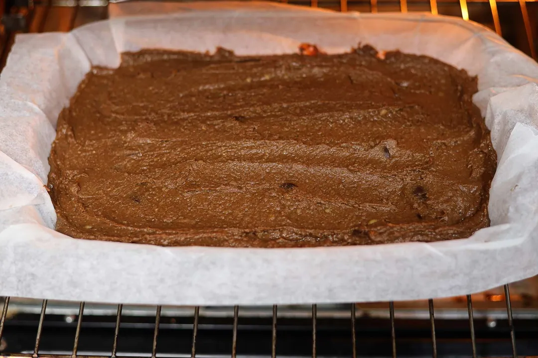 A baking tray lined with parchment paper that's been filled with brownie batter baking in the oven.